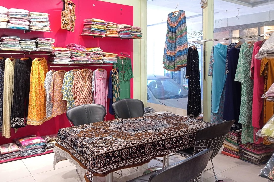 Inside Neetu Fashion: shelves of folded suits and dupattas, racks of printed kurtis and long dresses against a pink wall